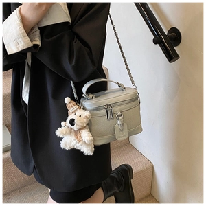 Detail of sage green quilted box bag with metal chain strap and plush bear charm decoration