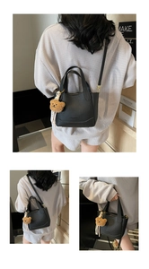 Detail of black lychee grain bucket bag with a cute brown plush bear charm and strap