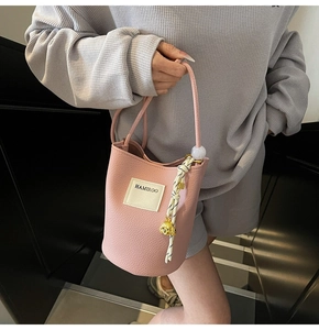 Détail du sac seau rose à motif litchi avec lanière tissée et breloque tête de chiot