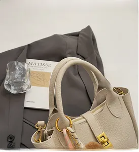 Detail of cream lychee leather bucket bag with gold hardware and plush charm decoration