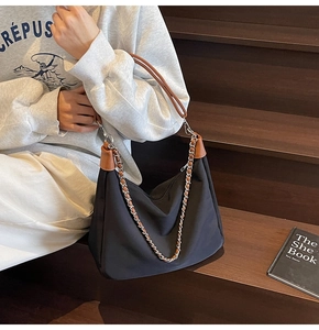 Detail der schwarzen Shopper-Tasche mit braunen Ledergriffen und Silberkette am Modell