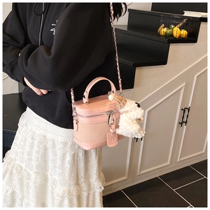 Detail shot of a pink box bag with woven texture, metal chain strap, and plush puppy charm