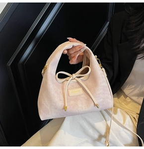 Detailed view of light pink handbag with vertical texture, bow decoration and gold hardware