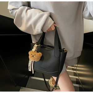 Detail of black lychee texture leather bucket bag featuring a cute plush bear charm