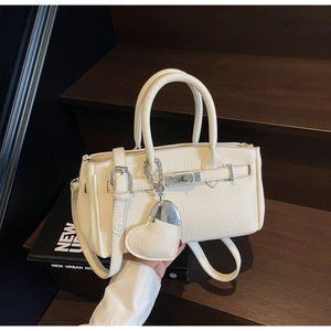 Detailed close-up of cream-white litchi grain leather bag with heart charm and silver lock