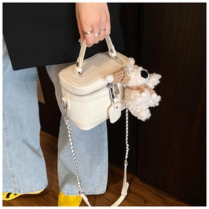 Detail view of cream box bag with woven texture, silver chain and plush puppy charm