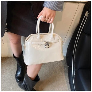 Detailed view of the cream glossy seashell handbag with silver metal buckle held by hand
