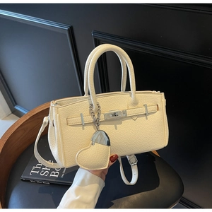 Detail view of lychee-textured off-white leather handbag with heart-shaped charm and silver lock