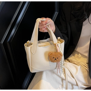 Detail of off-white lychee texture leather bucket bag with cute bear charm and silk scarf