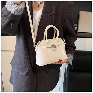 Close-up of cream shell bag with metallic lock detail and glossy oil wax leather finish