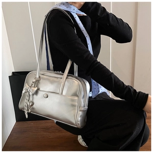 Detail view of silver metallic Boston bag with long handles and heart-shaped charm