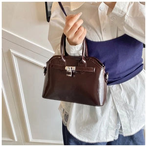 Close-up of brown glossy oil-wax leather shell bag with metal buckle and top handles