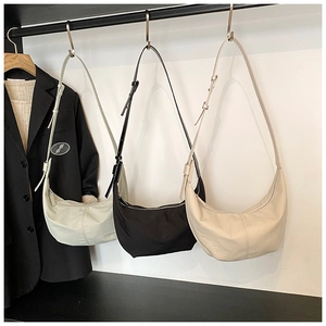 Three minimalist half-moon shoulder bags in green, black, and beige hanging with a blazer