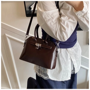 Detail of dark brown glossy leather satchel featuring silver metal buckle and top handle