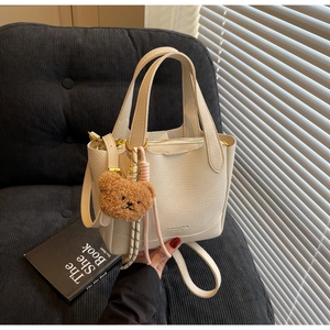 Detail of off-white lychee texture tote bag with a cute bear charm on a black sofa