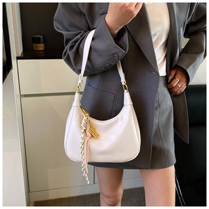 Detail of a creamy white moon-shaped hobo bag with a gold abacus charm and braided tassel