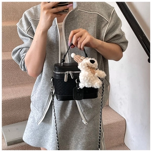 Detail of black quilted box bag with chain strap and cute bear plush charm accessory