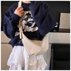Detail view of the cream crescent bag showing the adjustable wide strap and texture