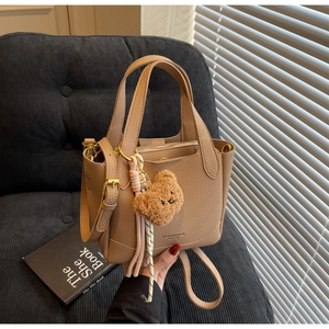 Close-up of khaki pebbled leather bucket bag with cute bear charm on a grey sofa