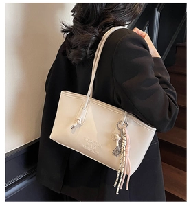 Detail view of beige leather bucket bag with embossed logo and braided tassel ornament