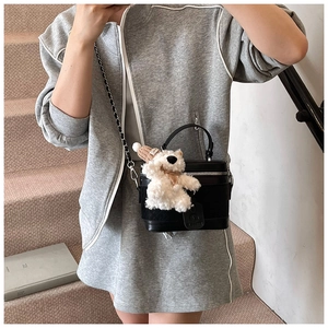 Detail of black box bag with chain strap and cute teddy bear charm on model