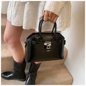 Detail of a black oil-wax leather shell bag with silver buckle and polished finish