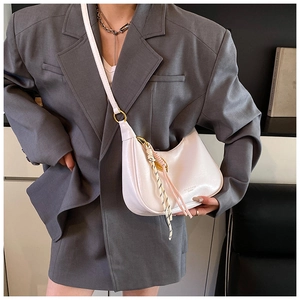 Close-up of white half-moon shoulder bag with gold hardware and tassel detail on model