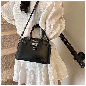 Detail of black glossy shell handbag with metal padlock and elegant leather straps