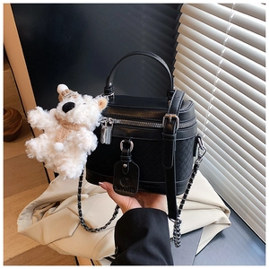 Detail of black box handbag featuring woven texture and a cute teddy bear charm