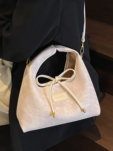 Elegant beige tote bag with bow detail and textured fabric worn on dark clothing