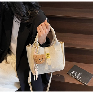 Detailed close-up of white lychee textured bucket bag with gold lock and bear charm
