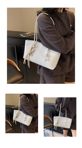Detail view of large grey tote bag with thin shoulder straps and tassel accessory