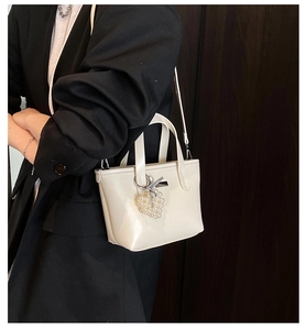 Detail of cream white bucket bag with pearl heart charm and ribbon on black blazer