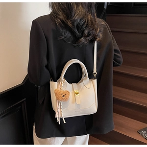 Detail view of beige lychee pattern leather bucket bag with a cute brown plush bear pendant