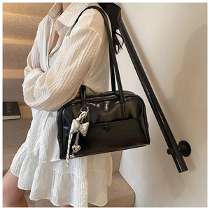 Detail of glossy black Boston bag with silver bow and heart pendant on a model