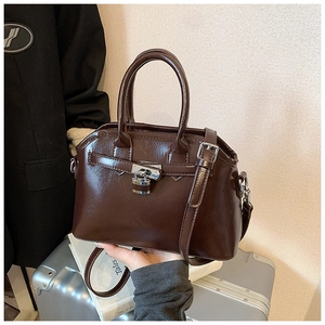 Detailed view of deep brown oil wax leather handbag with metal lock and luggage accessory