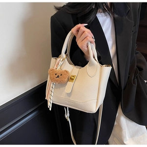 Detail of cream lychee texture handbag featuring a cute plush bear charm and gold buckle