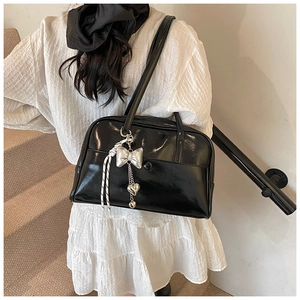 Detail of black patent leather shoulder bag with silver bow charm and heart pendant