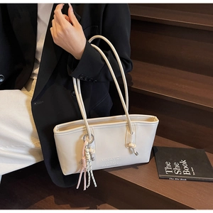 Detail of cream bucket bag with embossed logo, knotted cord, and pink tassel charm