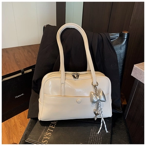 Detail of a creamy white Boston bag with a silver butterfly charm and tassels