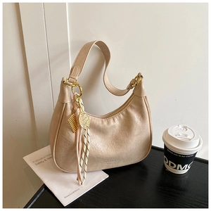 Detail of beige hobo tote bag featuring gold hardware and a tennis racket charm accessory
