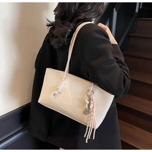 Detail view of cream bucket bag with embossed logo and decorative tassel ornament