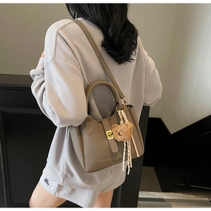 Close-up of litchi grain bucket bag with gold clasp and plush bear charm on a model