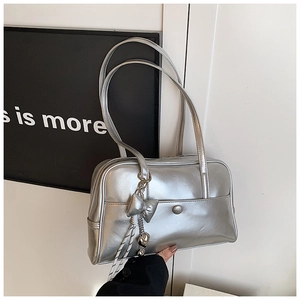 Close-up of silver Boston bag with metallic finish, bow charm, and heart pendant detail