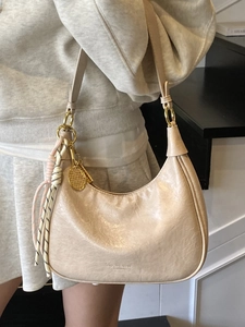 Chic beige waxed leather crescent bag with gold hardware and tennis racket charm pendant