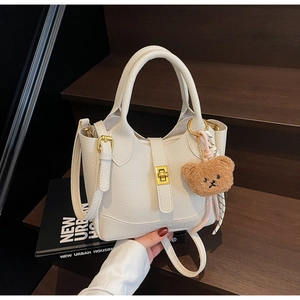 Close-up of white lychee pattern leather bucket bag with golden buckle and bear charm