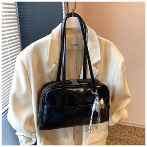 Detail of glossy black patent leather Boston bag styled on a blazer with a silver bow charm