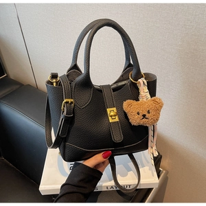 Detail of black lychee grain leather bucket bag with gold lock and bear pendant charm