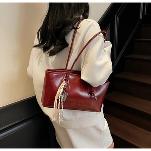 Detail of burgundy leather shoulder bag with embossed letters and braided tassel charm