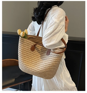 Detail view of large straw tote bag with brown leather handles worn by a model in white dress